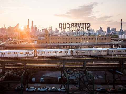Queens, New York, USA - July 23,2021: Aerial of New York subway running on an elevated railway track in Queensboro with view of Manhattan skyline during sunset