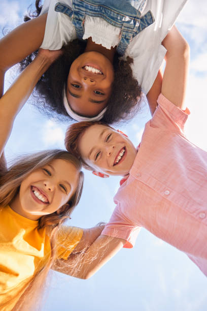 Company of diverse children embracing together against blue sky stock photo