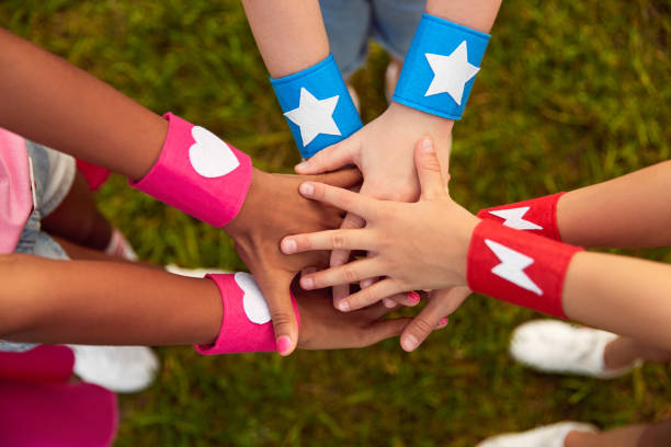 Diverse children with superhero bracelets stacking hands From above of group of crop anonymous multiethnic friends with colorful superhero bracelets stacking hands while playing together in summer park stacked hands photos stock pictures, royalty-free photos & images
