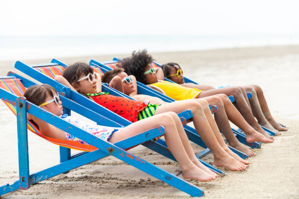grupo de niños de la diversidad acostados en silla de playa juntos en la playa en vacaciones de verano - sólo niñas fotografías e imágenes de stock