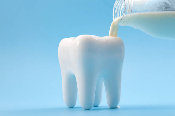 Oral health, cavity prevention and calcium rich drink for strong teeth concept with glass bottle pouring milk into a heathy tooth isolated on blue background Oral health, cavity prevention and calcium rich drink for strong teeth concept with glass bottle pouring milk into a heathy tooth isolated on blue background glass medicine blue bottle stock pictures, royalty-free photos & images