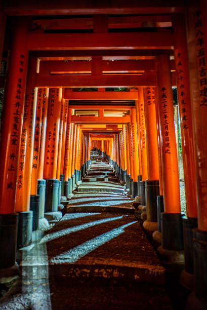 Fushimi Inari a historical Japanese shrine in Kyoto Japan.  A serene zen walk down a stone path past the many red Shinto torii gate in the morning and evening.  The mood is alway tranquil weather lit by the sun beams at dawn or shadowy corners created by the lanterns at night.
