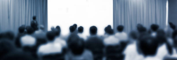 istock Blurred de-focused audience in conference lecture presentation room. Corporate presentations in conference hall. Seminar speaker giving training to new employees. Presenter in forum workshop event. 1391133736