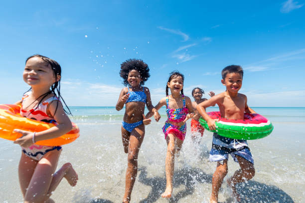 grupo de niños de la diversidad jugando juntos en la playa tropical en las vacaciones de verano en el mar - floatation device fotografías e imágenes de stock