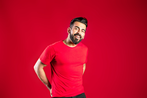 The shot of a confident Indian man in red t-shirt looking to camera with red background.