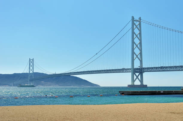il ponte akashi-kaikyo, il ponte sospeso più lungo del mondo, cielo blu e spiaggia sabbiosa. - kobe bridge japan suspension bridge foto e immagini stock