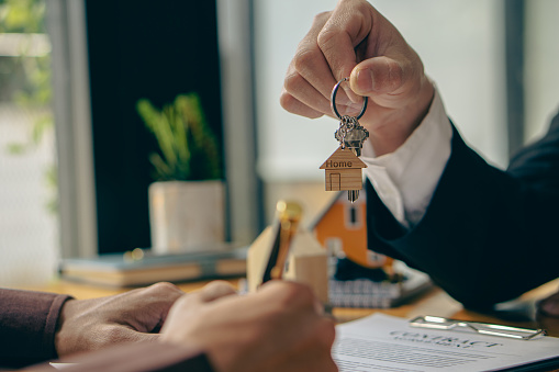 Sales representatives offer home purchase contracts to purchase a house or apartment and give home key chains to customers in the office buying or selling and renting real estate ideas.