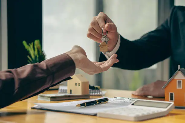 Photo of Sales representatives offer home purchase contracts to purchase a house or apartment and give home key chains to customers in the office buying or selling and renting real estate ideas.