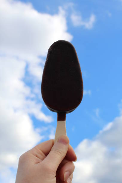 mano della donna con gelato al cioccolato sullo sfondo del cielo con le nuvole. - creamsicle foto e immagini stock