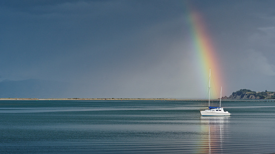 Rainbow over a yacht, Motueka seafront, the Motueka sandspit in the background, Motueka, Tasman region, south island, Aotearoa / New Zealand.