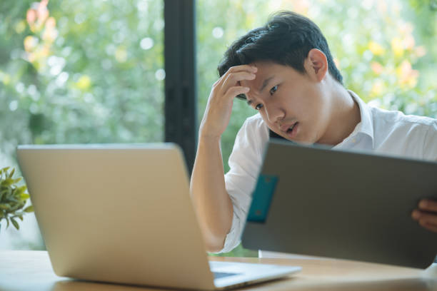 istock Asian man working busy while making phone call and using laptop at home 1391148003