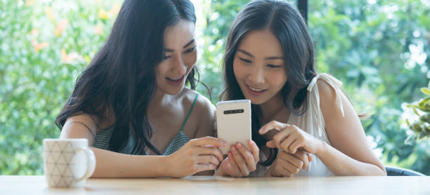 istock Two Asian friends using mobile phones together while sitting at the cafe 1391148012