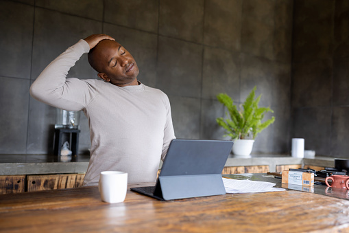 African American man working at home and stretching his neck during an active pause