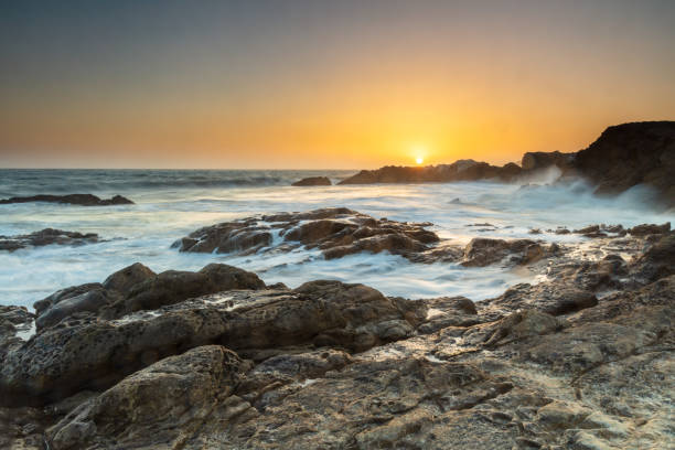 istock Sunset on rocky beach. Silky water, orange sun. Cliffs in distance. 1391152145