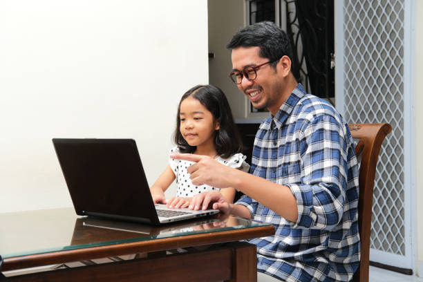 Asian father and his daughter looking to the laptop screen with happy face Asian father and his daughter looking to the laptop screen with happy face keluarga stock pictures, royalty-free photos & images