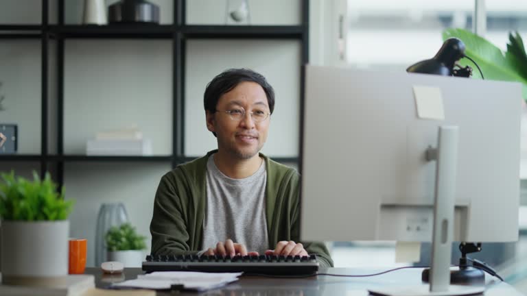 Mid adult man working at home on holiday,Home Office: a Happy Young Asian freelance creative man Working in the Comfort of His Home, Social Distancing Concept