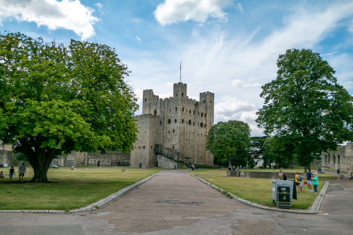 People walking around while visiting Rochester Castle in Kent. Opened in 1087, this castle was built in the Norman style. It was built from Kentish ragstone and the keep and tower date back to the 12th century. Entry into the castle is charged. On the left is Rochester Cathedral.