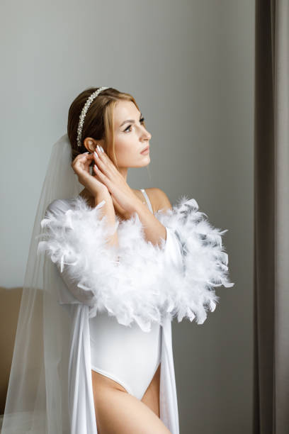 hermosa novia hermosa con túnica de seda posando cerca de la ventana con luz suave por la mañana. - veil bride human face wedding fotografías e imágenes de stock