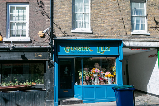 Many goods for sale in the store window of Ginger Lily Florist on Rochester High Street in Kent, England. Another shop with an alarm is also visible.