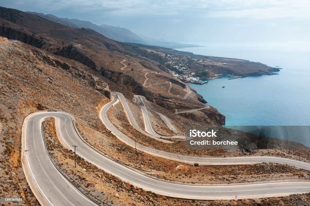 Curvy Mountain Road In Crete Aerial view on winding mountain road towards the sea in south Chania region (Crete, Greece). Crete Stock Photo