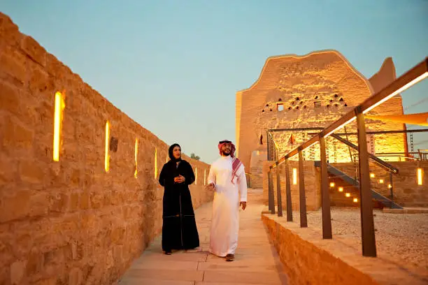 Full length front view of man and woman in traditional attire approaching camera as they walk through illuminated open air museum at dusk. Property release attached.