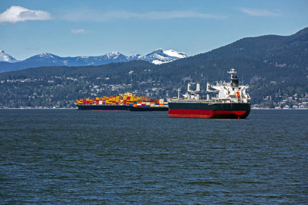 Ocean ships and container ships in Vancouver Harbor at a sunny  day against the backdrop of a snow covered  mountain ridge  and cloudy sky