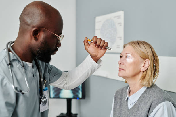 Young confident opthalmologist examining retina of mature female patient Young confident male opthalmologist in uniform examining retina of mature female patient with astigmatism with help of medical device retina stock pictures, royalty-free photos & images