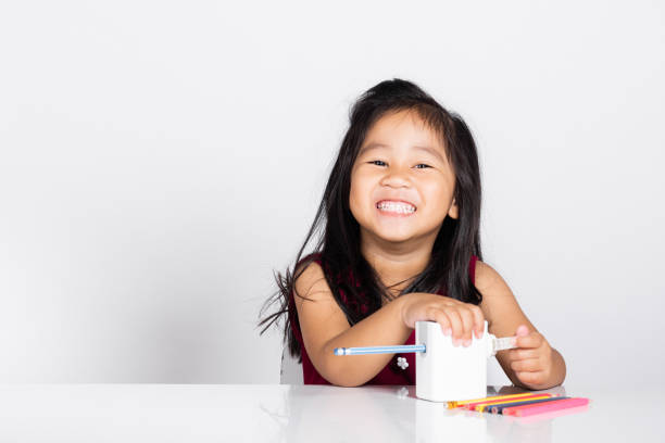 menina bonitinha de 3 a 4 anos sorri usando apontador de lápis enquanto fazia lição de casa em tiro de estúdio isolado - preschool 2 3 years preschooler little girls - fotografias e filmes do acervo