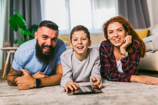 istock Happy family with one child lying on carpet and using digital tablet 1391167053