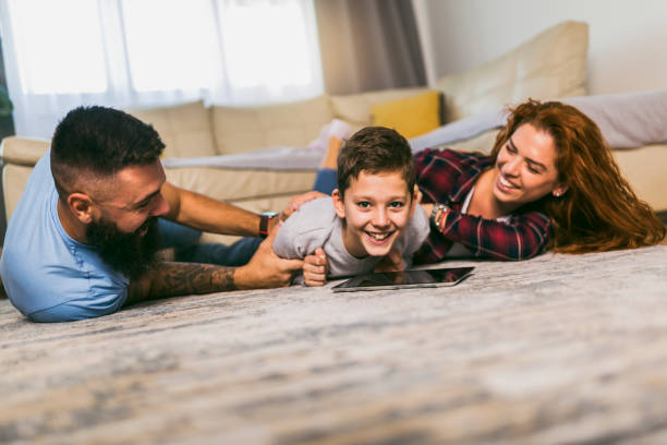 istock Happy family with one child lying on carpet and using digital tablet 1391167612
