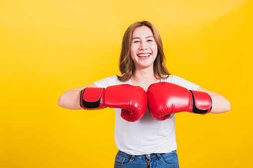 Portrait Asian Thai beautiful young woman standing smile wearing red boxing gloves and punch hand to hand, studio shot isolated on yellow background, There was copy space for text