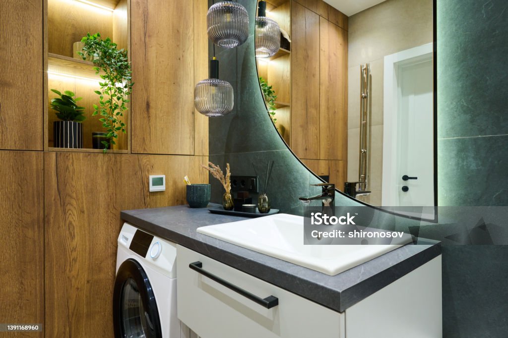 Part of bathroom with treetop green marble wall and wooden closet Part of bathroom with self care items, air freshener, washing machine and white sink between treetop green marble wall and wooden closet Bathroom Stock Photo