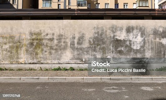 istock Grunge plaster wall  with moss and stains. Sidewalk and asphalt road in front. 1391170748