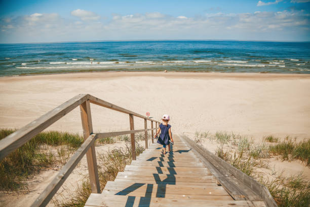 Little girl going down the stairs to the deserted sandy beach Rare view of a little girl going down the stairs to the deserted sandy beach on the Baltic sea baltic sea people stock pictures, royalty-free photos & images
