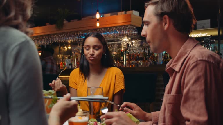 Diverse group of friends eating out at restaurant tasting food