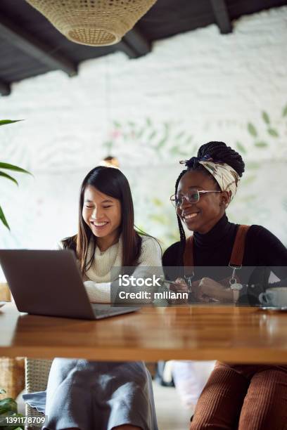 Two Multicultural College Girls Standing In The Cafeteria And Using A Laptop For Research Elearning And Data Availability Stock Photo - Download Image Now