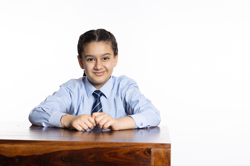 young girl of primary school sitting in classroom looking at the camera isolated on white background