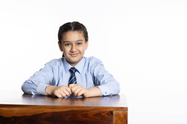 young girl of primary school sitting in classroom looking at the camera isolated on white background stock photo