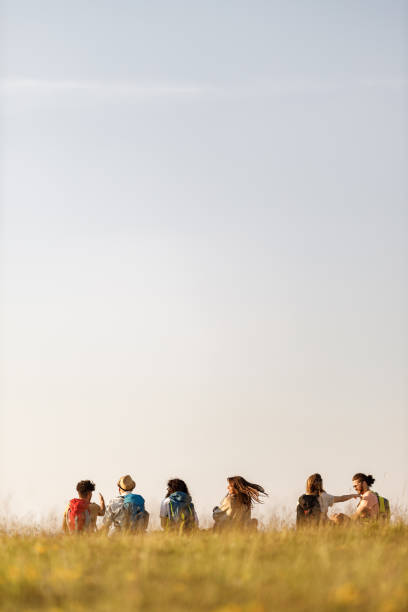 Rear view of large group of happy backpackers talking on a break at mountain. Copy space.