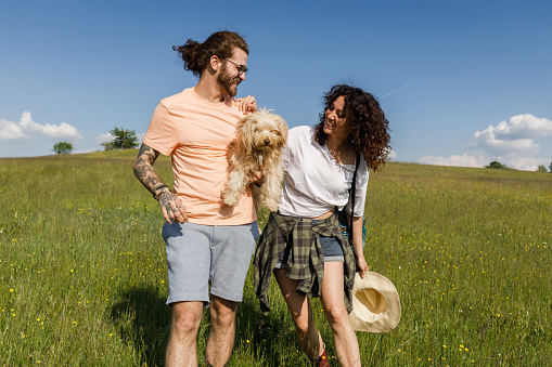 Happy couple and their dog walking down the hill during spring day in nature. Copy space.