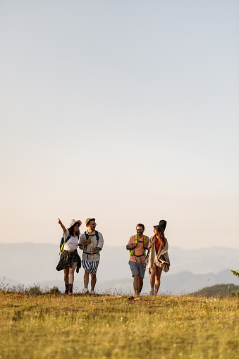 Happy couples of backpackers talking while walking in spring day on a mountain. One of them is aiming at distance. Copy space.