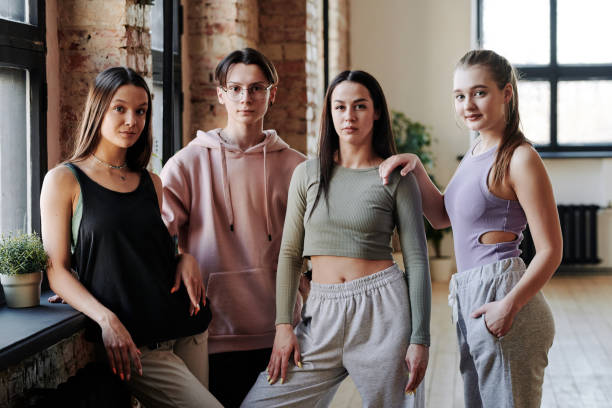 tres chicas adolescentes y un chico en ropa deportiva de pie en un moderno estudio tipo loft - common women teenage girls exercising fotografías e imágenes de stock