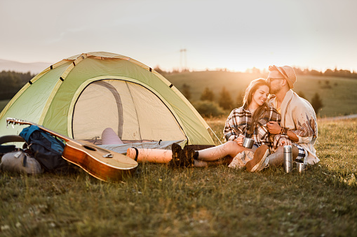Young happy woman enjoying in a kiss by her boyfriend during camping in nature at sunset. Copy space.