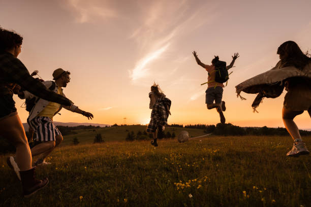 Group of playful backpackers having fun while running on a meadow at sunset. Copy space.