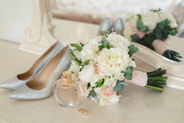 zapatos plateados de la novia, perfume, ramo y anillos de boda en el tocador cerca del espejo. - jewelry ring luxury wedding fotografías e imágenes de stock