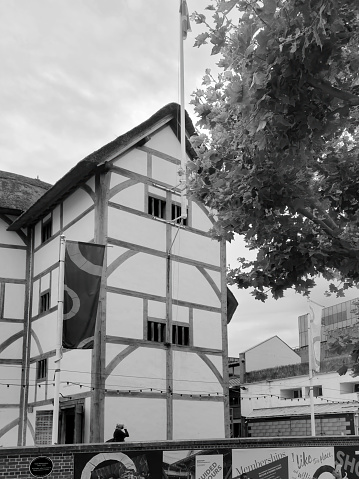 London, UK - August, 2021: The globe Shakespearean theatre on the south bank of the Thames. This shot is a wideangle view with flags and advertising visible and people in the foreground.