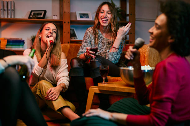 Two multicultural young women having fun at a home party while singing karaoke for their friends. stock photo