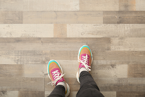 Woman in colorful sneakers standing on wooden floor, top view. Space for text