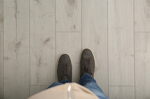 Person in brown shoes standing on wooden floor, top view. Space for text