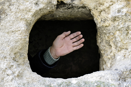 Male hand is visible from the hole in the stone rock. Ancient half-destroyed synagogue. The texture of the old dilapidated masonry. Place for religious rituals. Rashkov, Moldova. Selective focus.